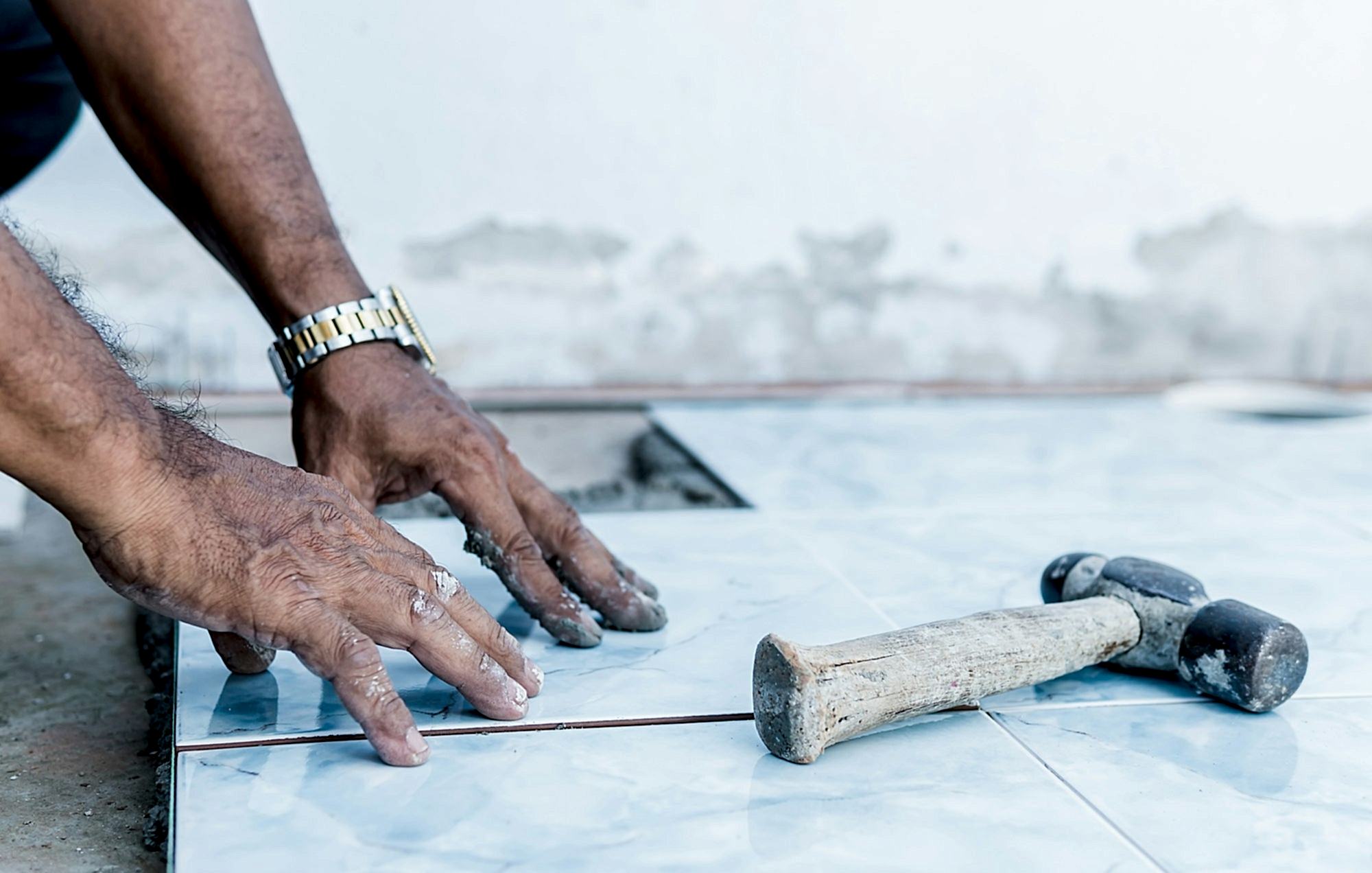Hand worker flooring ceramic tile and hammer